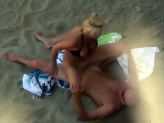 Voyeur en la playa con la cámara de vídeo graba una pareja follando en la arena